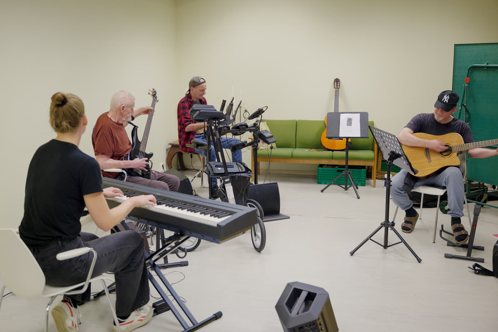 Gruppebilde av en et band som øver. Tre menn og en dame med ulike instrumenter øver på å spille sammen. Fotografi.